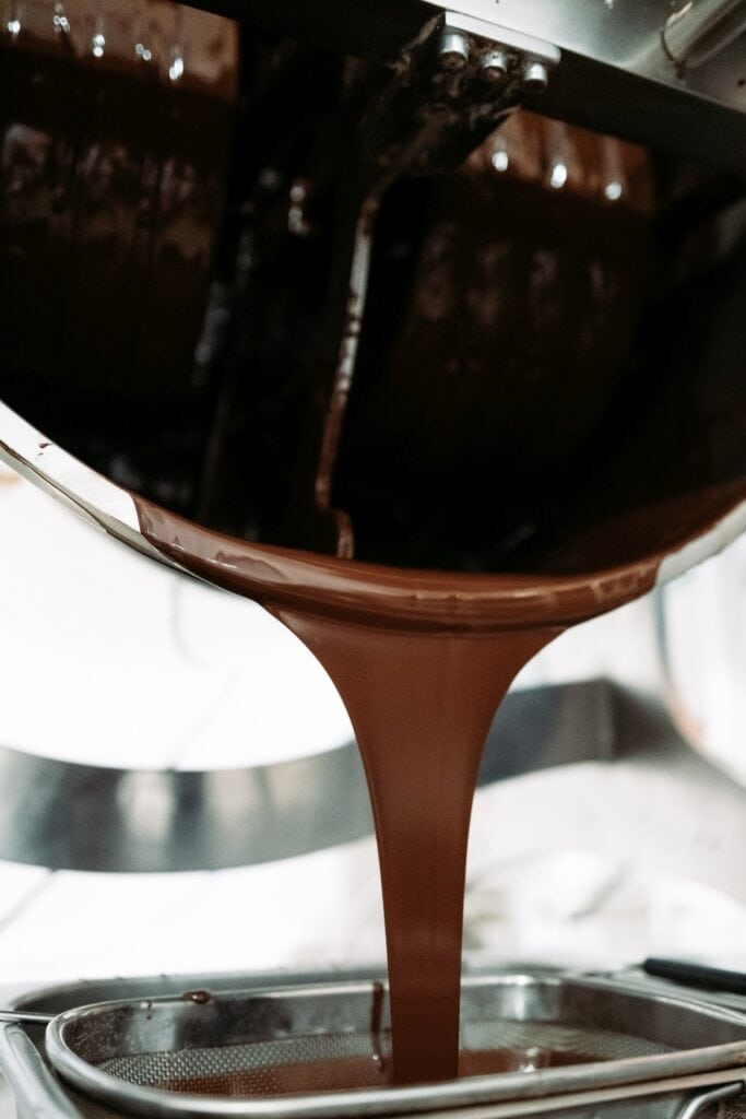 Flüssige Schokolade wird aus einer Schüssel in ein Sieb gegossen.