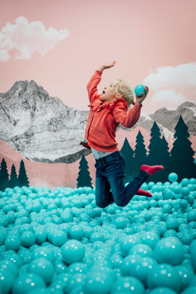 A child jumps out of a ball pool with turquoise balls