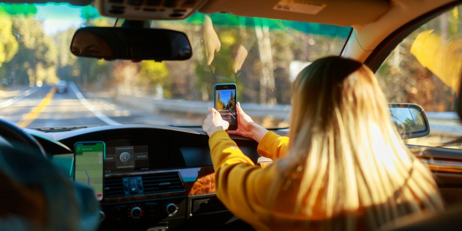 Eine Beifahrerin hält im Auto ein Smartphone an die Windschutzscheibe und macht ein Foto
