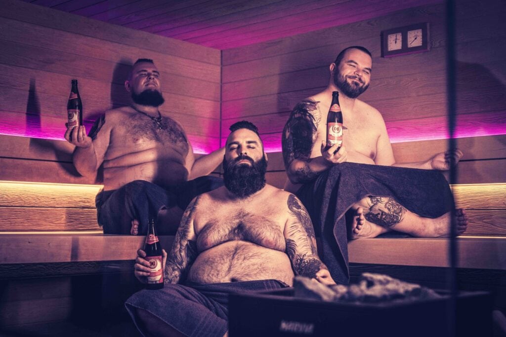 Drei Männer sitzen mit Bier in einer Sauna