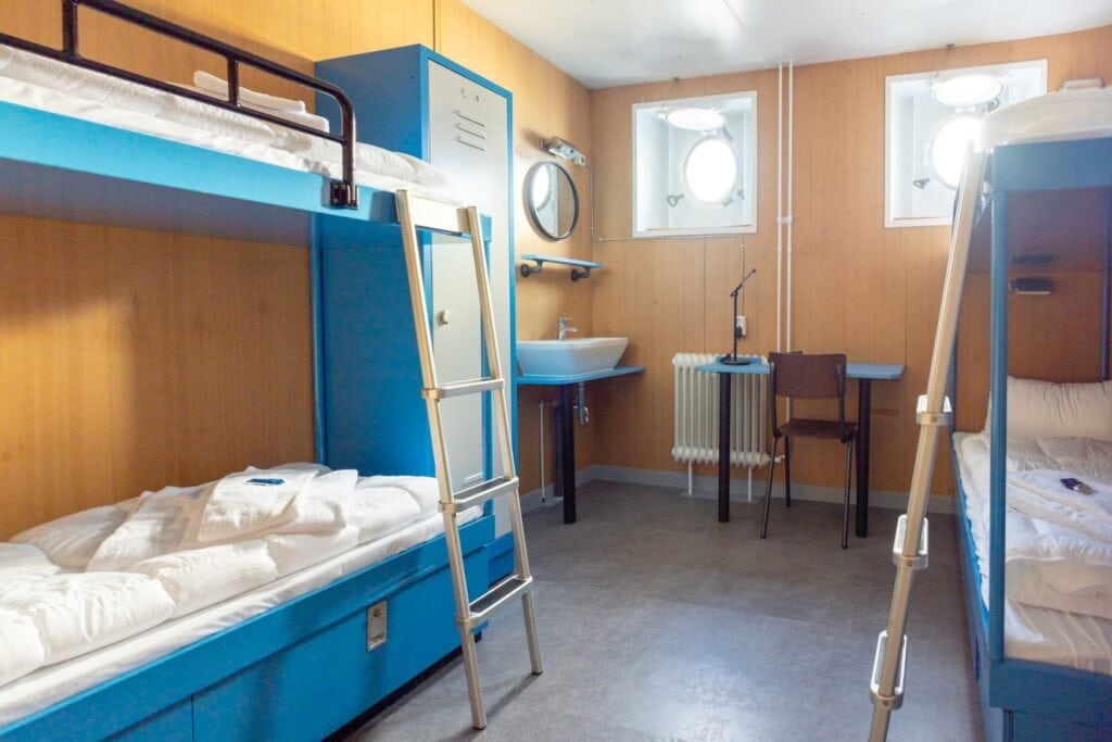 Eine Kajüte auf dem Hostel-Schiff Arcona an der Nordsee, mit blauen Doppelbetten und einem Bullauge