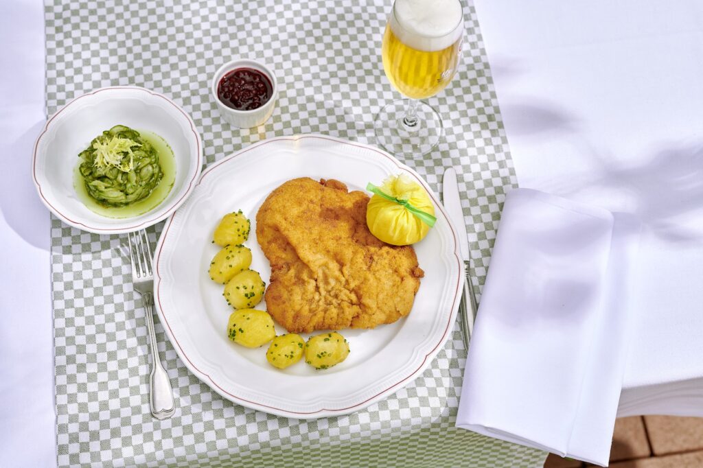 Schnitzel with potatoes on a plate, accompanied by a beer, served together in style on a country house table with a chequered tablecloth