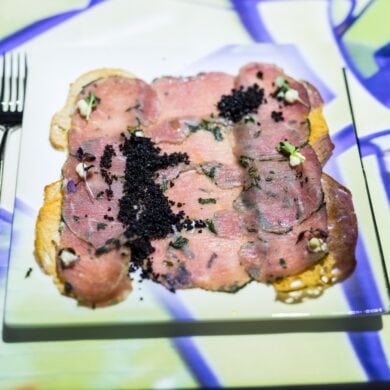 A plate of densely arranged carpaccio on an art-lit table