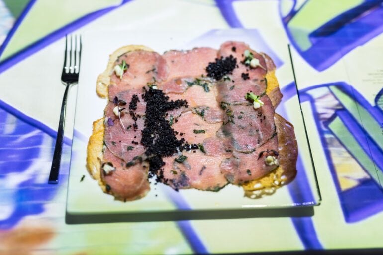 A plate of densely arranged carpaccio on an art-lit table
