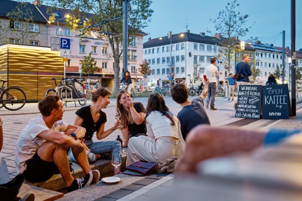 Menschen sitzen im Sommer an einem der Freiburger Bächle