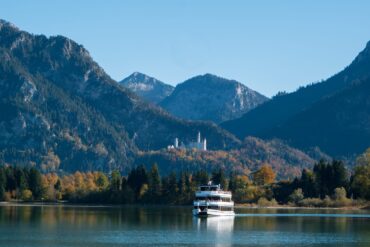 Auf dem Forggensee bei Füssen fährt ein Ausflugsboot, im Hintergrund die Alpen