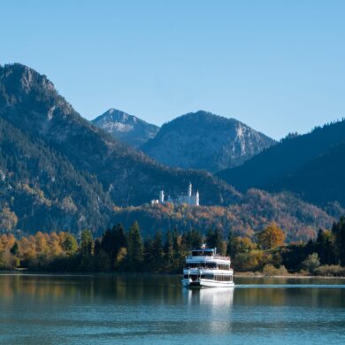 Auf dem Forggensee bei Füssen fährt ein Ausflugsboot, im Hintergrund die Alpen