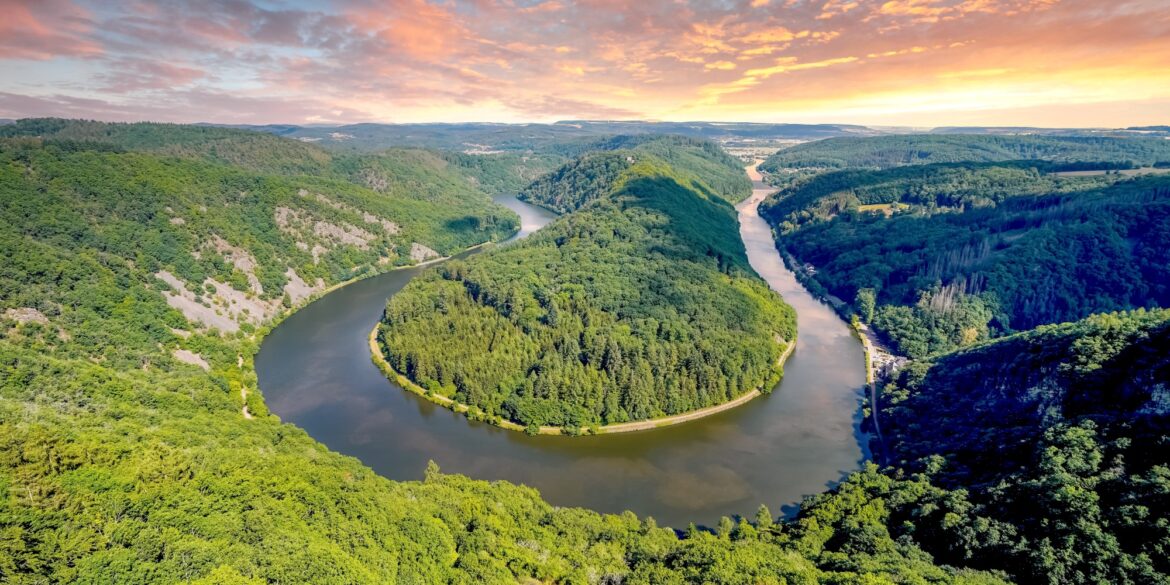 Blick auf eine Flussschleife in U-Form von einem hohen Aussichtspunkt. Die durch die Schleife gebildete Halbinsel ist ebenso bewaldet wie das gesamte Umland. Das Wasser ist spiegelglatt.
