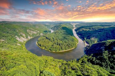 Blick auf eine Flussschleife in U-Form von einem hohen Aussichtspunkt. Die durch die Schleife gebildete Halbinsel ist ebenso bewaldet wie das gesamte Umland. Das Wasser ist spiegelglatt.