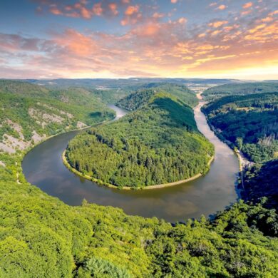Blick auf eine Flussschleife in U-Form von einem hohen Aussichtspunkt. Die durch die Schleife gebildete Halbinsel ist ebenso bewaldet wie das gesamte Umland. Das Wasser ist spiegelglatt.