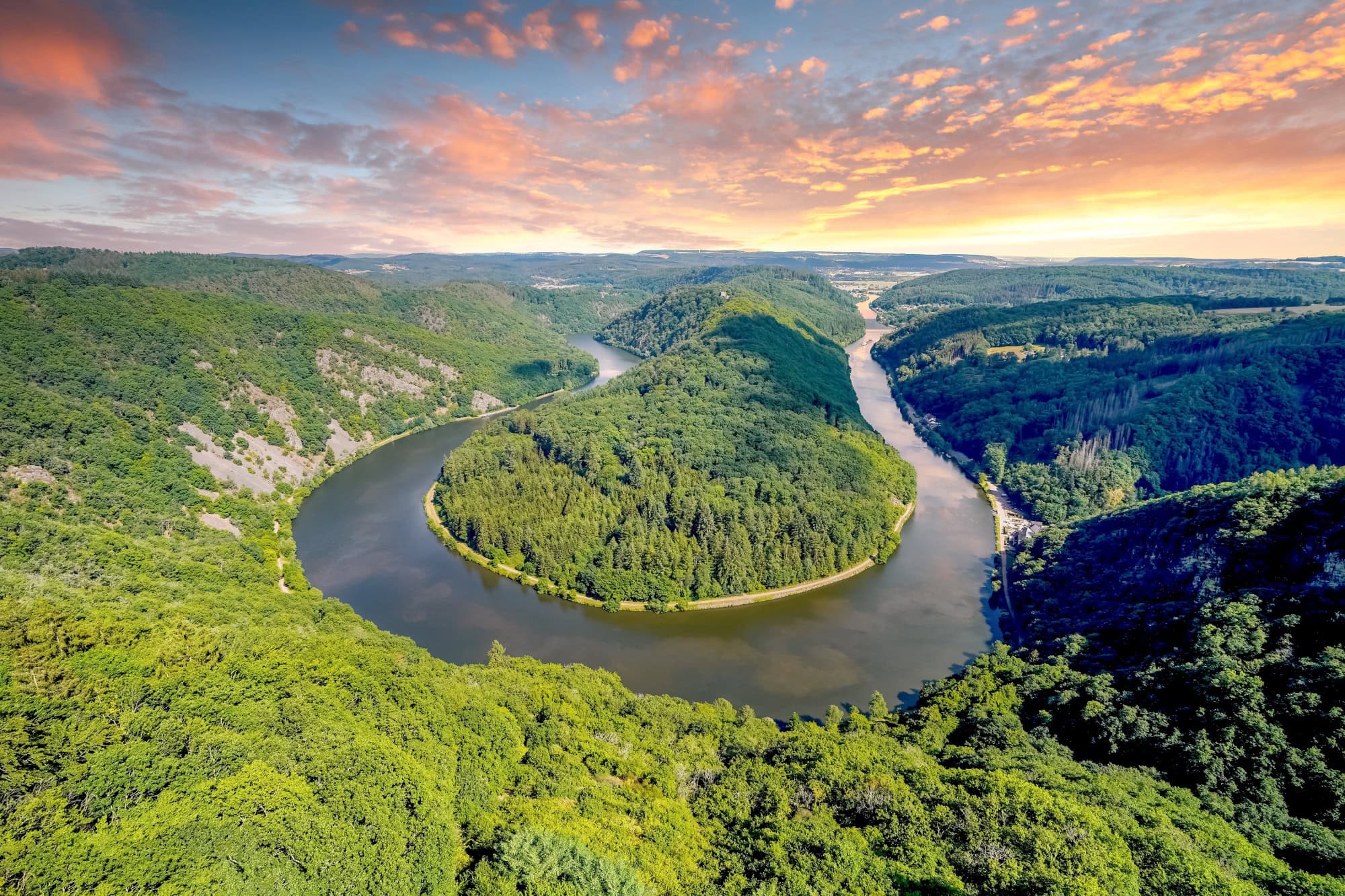 Blick auf eine Flussschleife in U-Form von einem hohen Aussichtspunkt. Die durch die Schleife gebildete Halbinsel ist ebenso bewaldet wie das gesamte Umland. Das Wasser ist spiegelglatt.