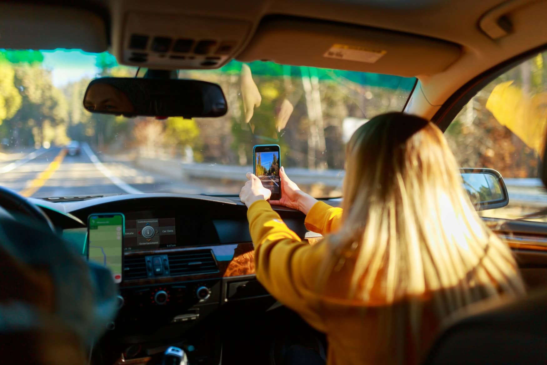 A passenger in the car holds a smartphone up to the windshield and takes a photo