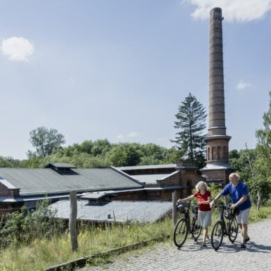 Two cyclists pushing their bikes in front of an industrial heritage site in Berlin