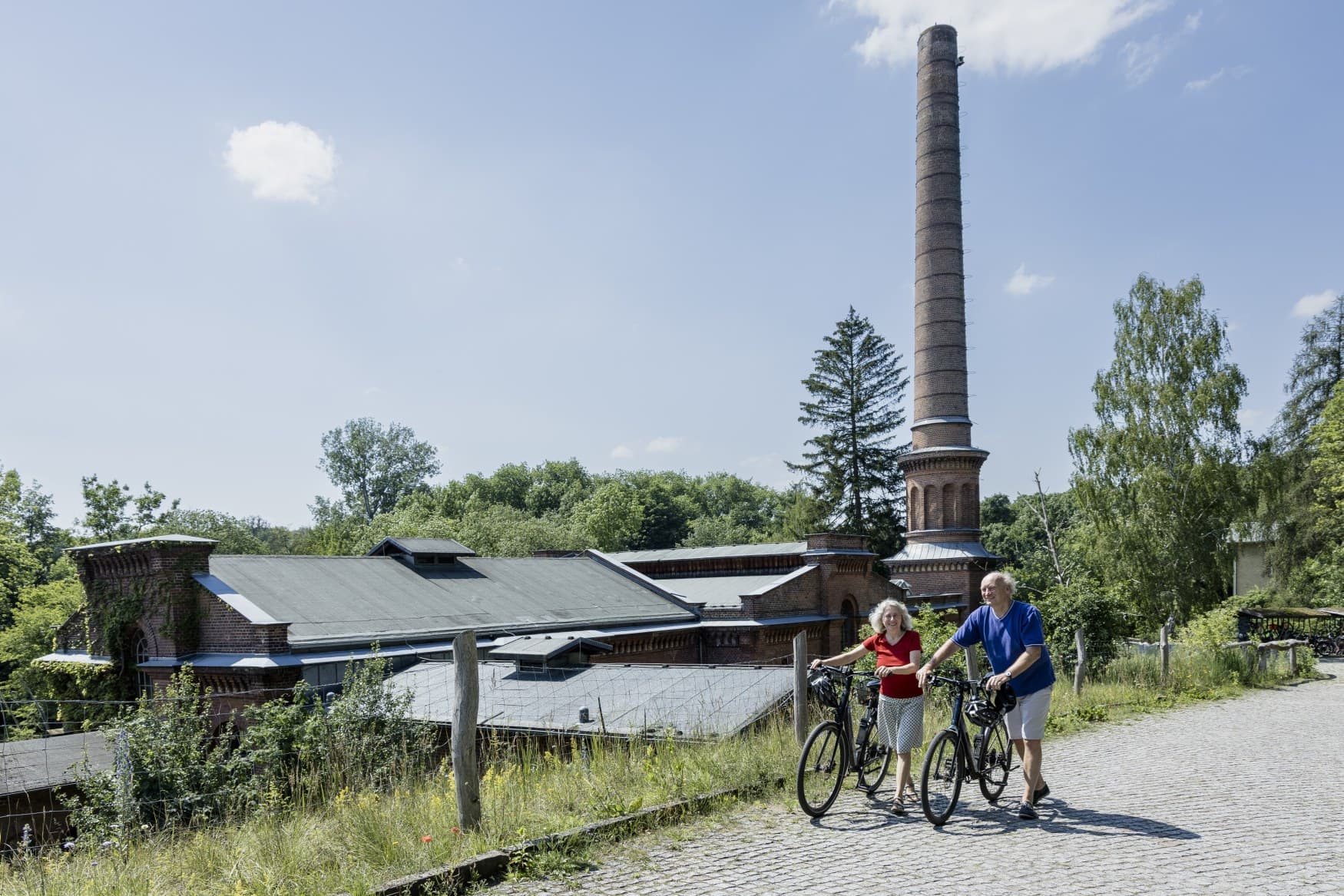 Two cyclists pushing their bikes in front of an industrial heritage site in Berlin