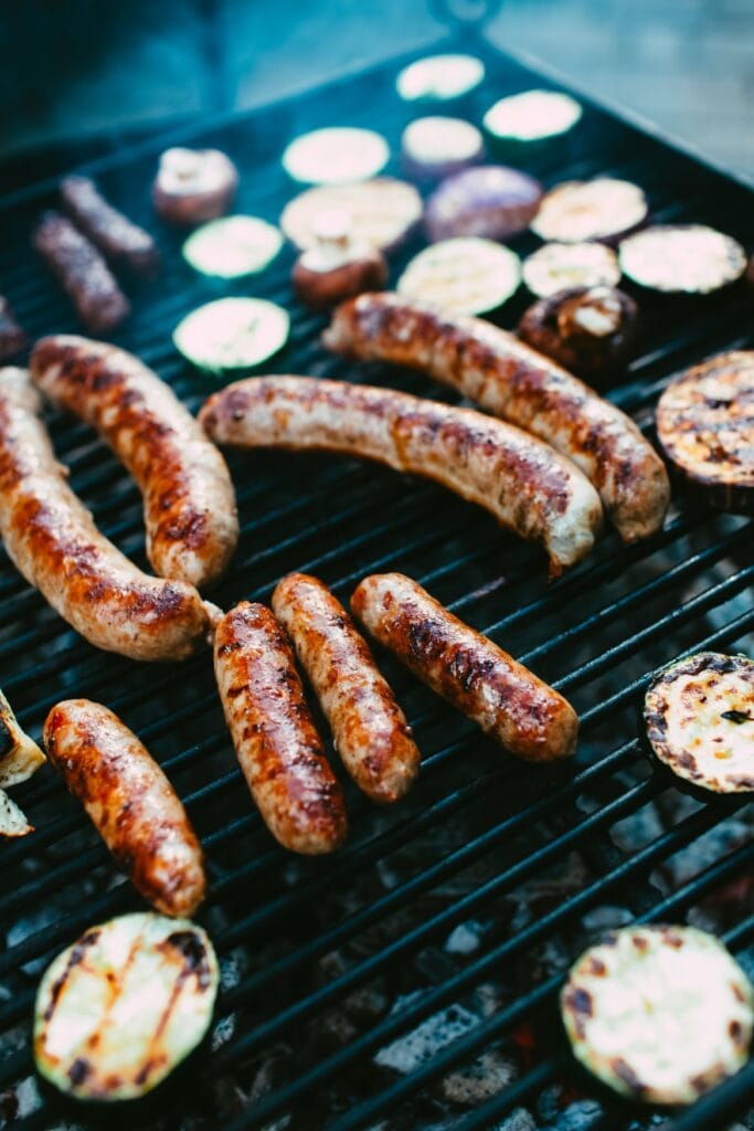 Auf einem Grillrost liegen Bratwürste und Zucchinischeiben