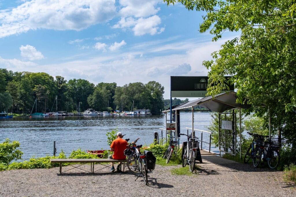 Ein Mann sitzt auf einer Bank an einem See, neben ihm steht sein Fahrrad