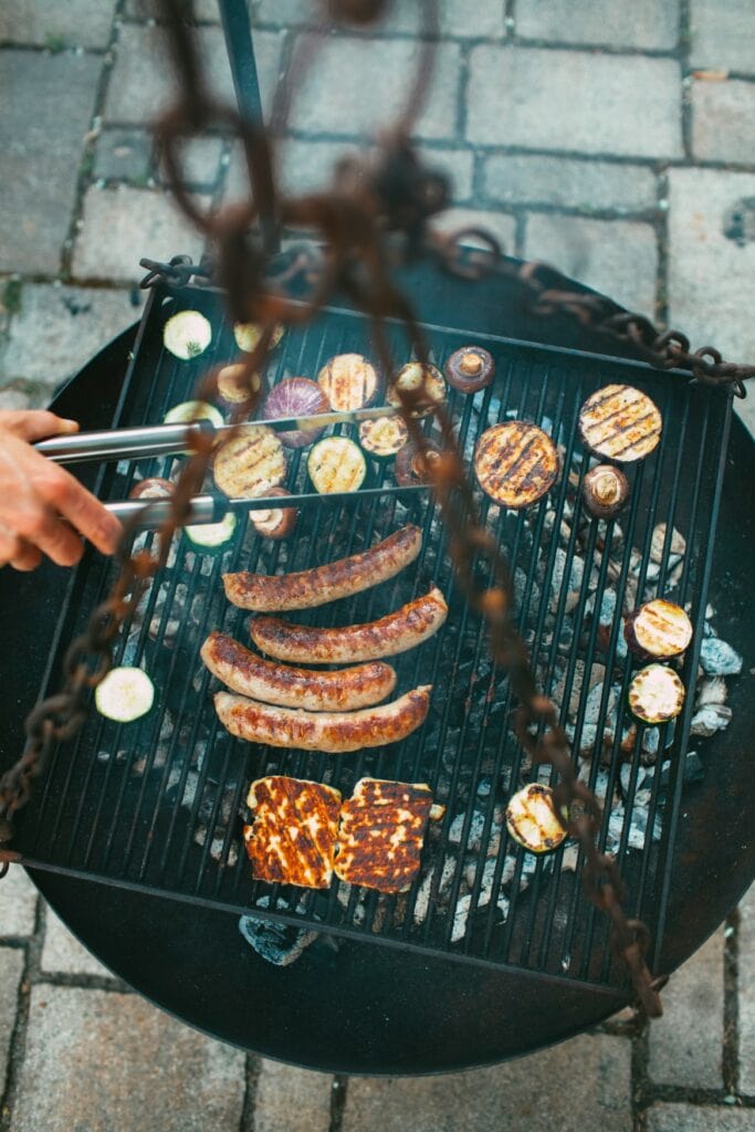 Eine Person wendet mit einer Zange Bratwürste auf einem Kohlegrill