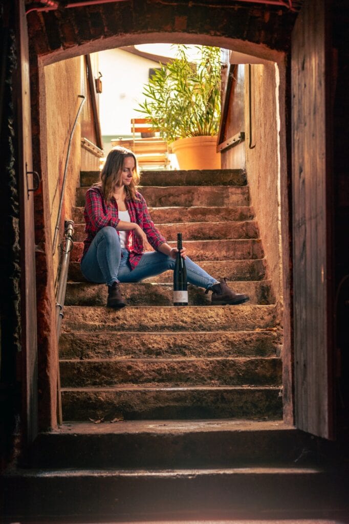 Lena Endesfelder sitzt auf der Treppe hinab zu ihrem Weinkeller, neben sich eine Weinflasche