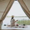 A woman sits in the entrance of a glamping tent and looks out over a lake