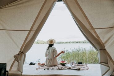 A woman sits in the entrance of a glamping tent and looks out over a lake