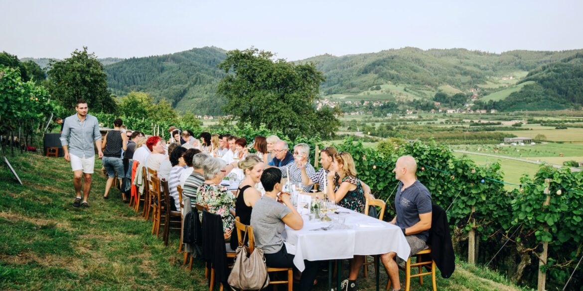 Eine Picknick-Gesellschaft sitzt an einem gedeckten Tisch auf einem Hügel, im Hintergrund idyllisches Schwarzwald-Panorama.