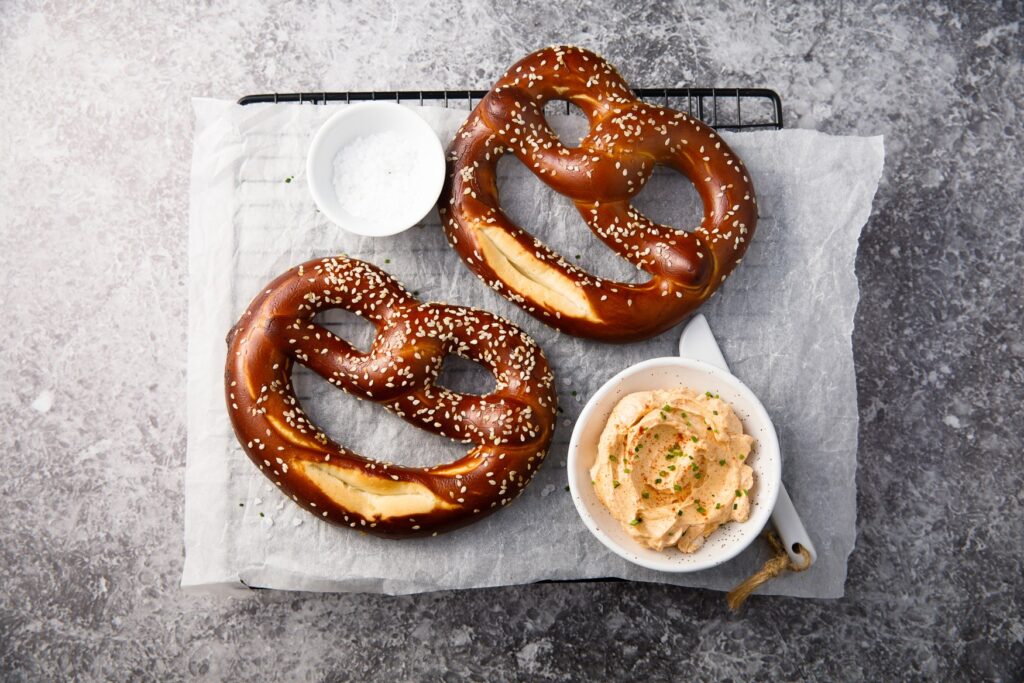 There are two pretzels and a bowl of Obazda on a tray