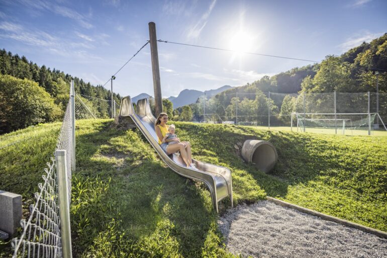 Eine Frau rutscht mit ihrem Kind auf einem Spielplatz im Chiemsee-Alpenland