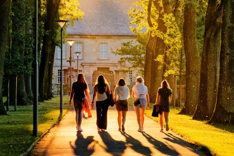 Five women walk through a park in the sunshine