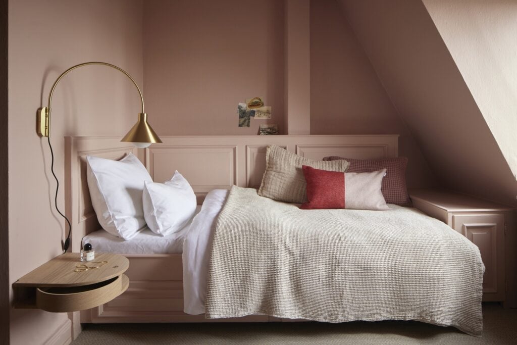 Ein hell-mauve-farbenes Zimmer im stilwerk Blankenese. Das Bett steht mit der Seite zur Wand und kann so auch als Sofa genutzt werden