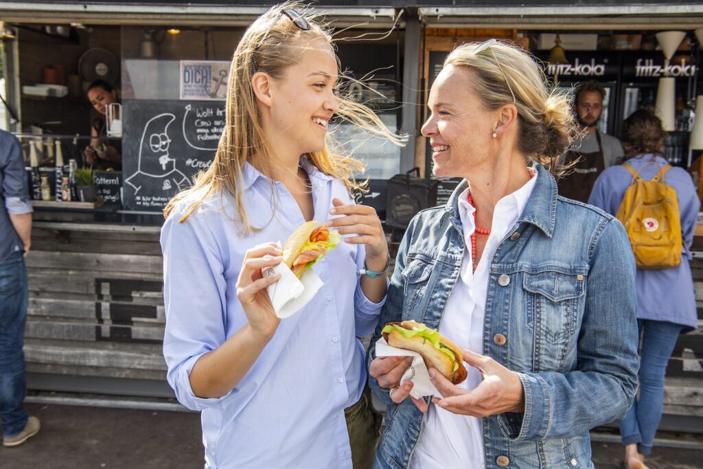 Two women holding vegan fish sandwiches in front of the fish bar in Nienhus