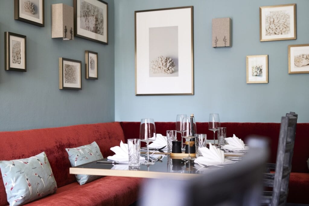 Eine Sitzecke mit rot gepolsterter Bank und vielen maritimen Bildern an der Wand im Restaurant des Strandhotels Zingst