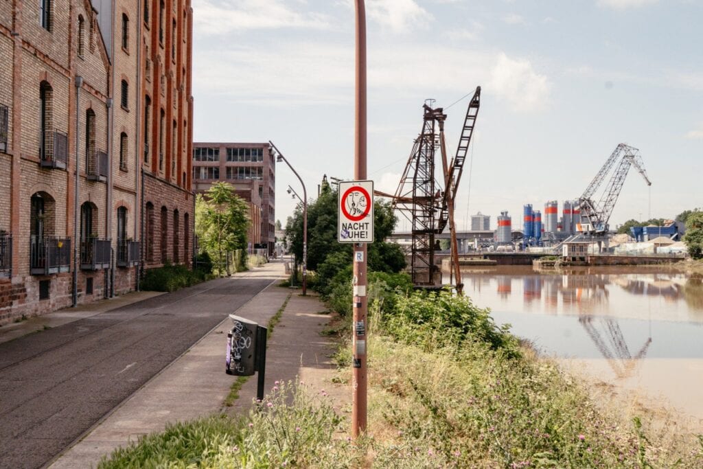 Ein Schild mit Aufschrift "Bitte Nachtruhe" steht am Ufer des Mannheimer Hafens, links ein Backsteingebäude