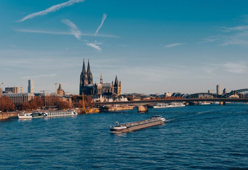 Blick auf die Deutzer Brücke in herbstlicher Abendsonne, im Hintergrund der Dom, im Vordergrund ein Frachter auf dem Rhein