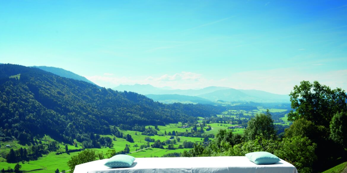 Vor einem malerischen Alpenpanorama steht eine Wellnessliege im Freien