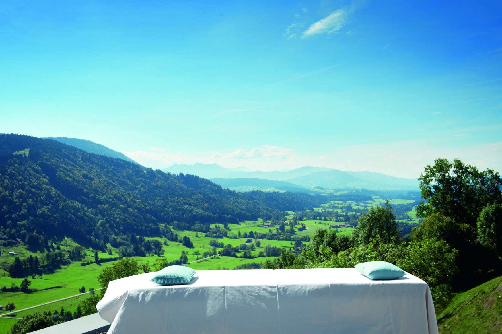 Vor einem malerischen Alpenpanorama steht eine Wellnessliege im Freien