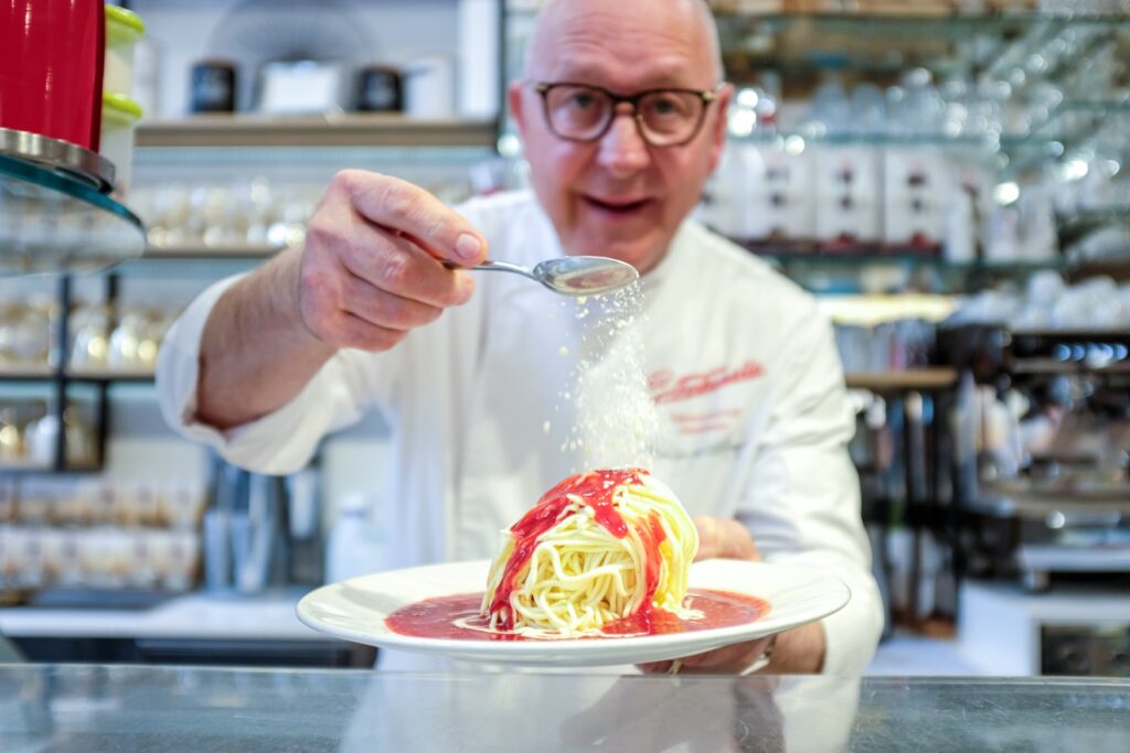 Dario Fontanella sprinkles white chocolate on a spaghetti ice cream