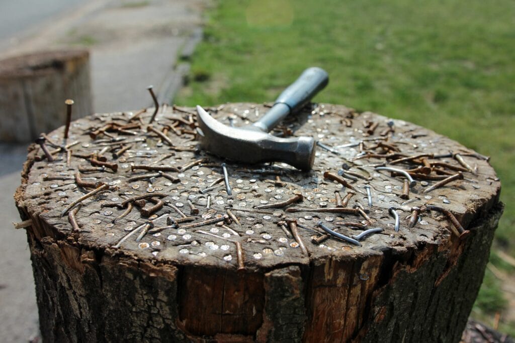 Auf einem mit Nägeln übersähten Baumstumpf liegt ein Hammer