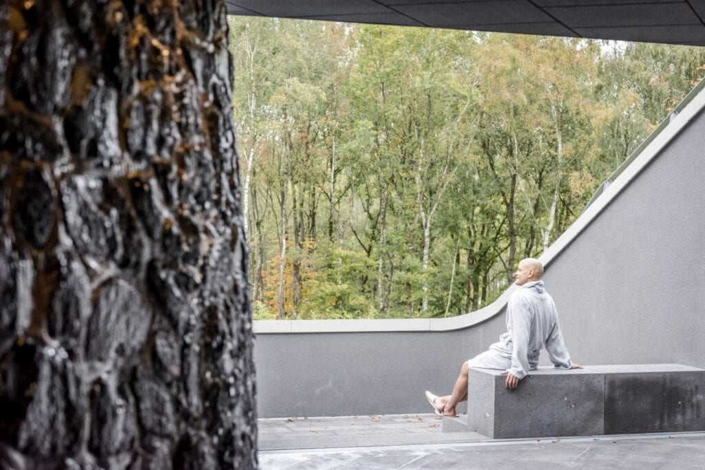 Ein Gast in der Seezeitlodge blickt von einer Bank auf den umliegenden Wald