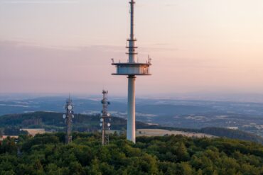 Drohnenaufnahme des Funkturms auf dem Vogelsberg in Hessen, im Hintergrund scheint sanft das Licht der Abenddämmerung