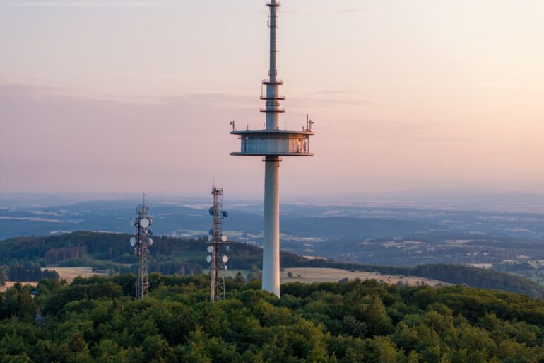Drohnenaufnahme des Funkturms auf dem Vogelsberg in Hessen, im Hintergrund scheint sanft das Licht der Abenddämmerung