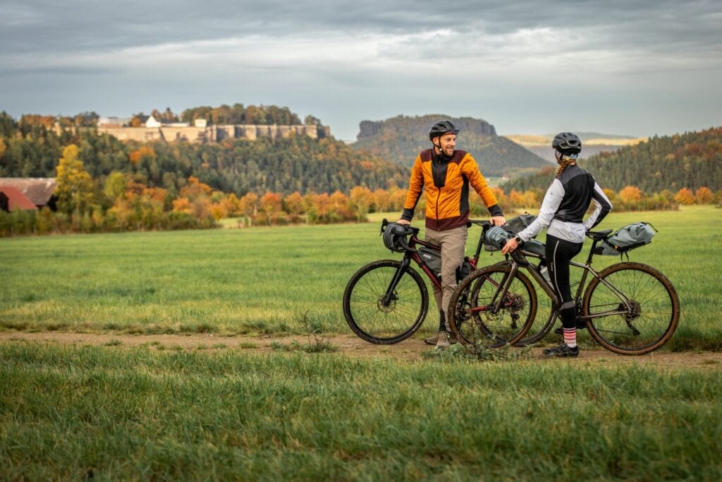 Zwei Radler in der Sächsischen Schweiz machen eine kurze Pause, im Hintergrund liegt die Festung Königstein