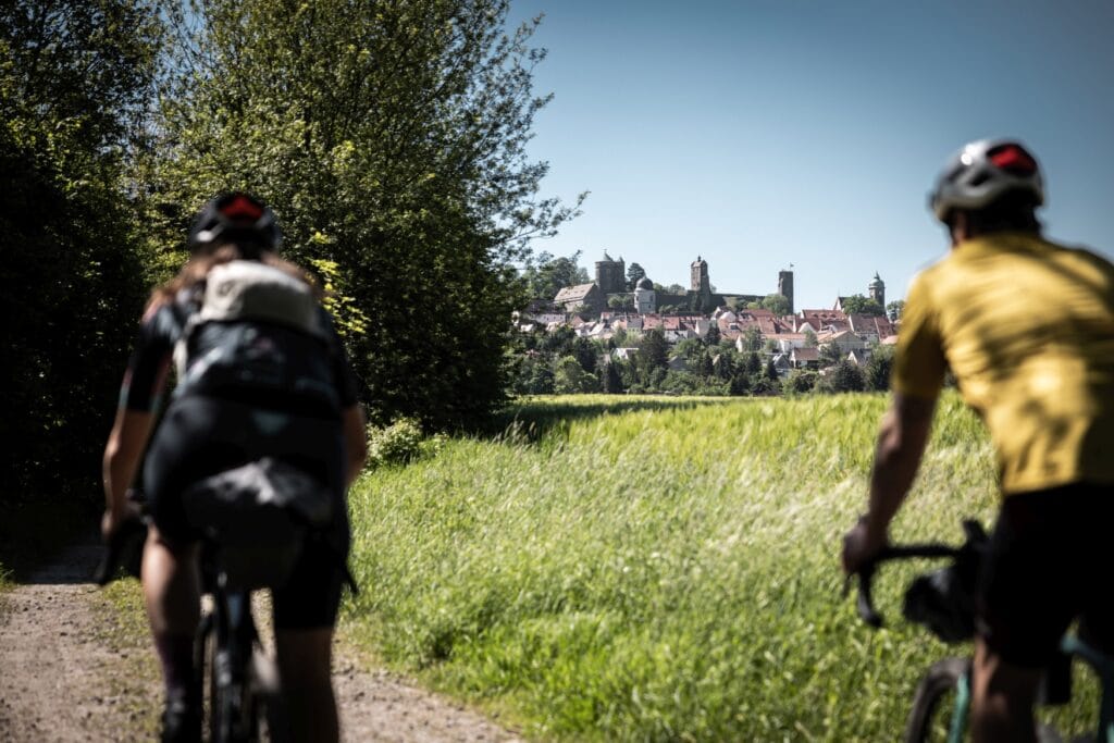 Zwei Radler fahren in Richtung der Stadt Stolpen, die im Hintergrund zu sehen ist