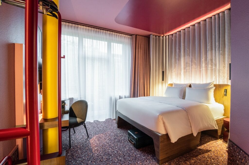 Ein Zimmer in der Hotelneueröffnung Tribe in Düsseldorf, mit Teppichboden, eleganter Beleuchtung und rosa Zimmerdecke