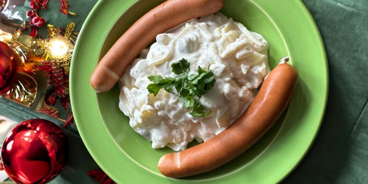 Eine Portion Kartoffelsalat mit zwei Bockwürsten, angerichtet auf einem weihnachtlich dekorierten Tisch