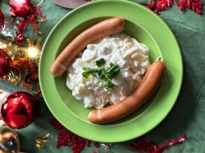 Eine Portion Kartoffelsalat mit zwei Bockwürsten, angerichtet auf einem weihnachtlich dekorierten Tisch