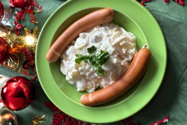 Eine Portion Kartoffelsalat mit zwei Bockwürsten, angerichtet auf einem weihnachtlich dekorierten Tisch