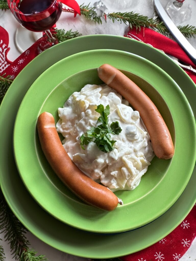 Eine Portion Kartoffelsalat mit zwei Bockwürsten, angerichtet auf einem weihnachtlich geschmückten Tisch