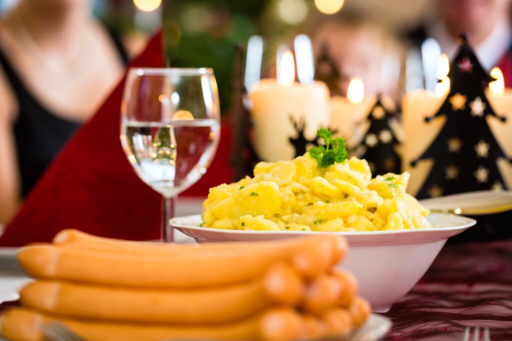 On a Christmas-decorated table, there is a plate of sausages and a bowl of potato salad.