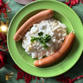 A portion of potato salad with two sausages, served on a festively decorated table