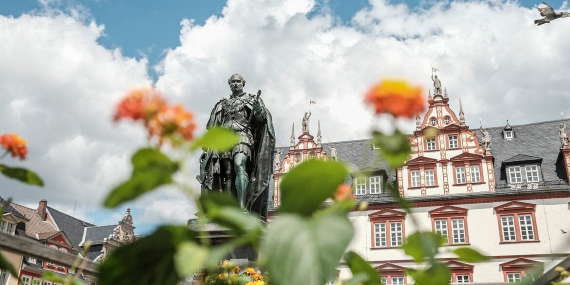 Eine Statue vor einem Haus mit Fachwerkelementen, davor Blumen